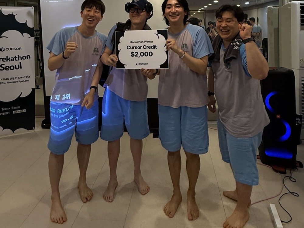 A winning team of four in sauna robes holding a Hackathon Winner board — $2,000 in Cursor credits